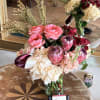 Pink and burgundy floral arrangement in a glass vase with cream hydrangeas