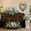 Casket surrounded by blue, white, and yellow funeral flower arrangements