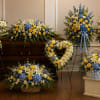 Funeral casket surrounded by blue, yellow, and white floral sprays