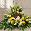 A low, elongated spray of yellow and white roses and lilies designed