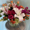 Mixed bouquet of white lilies, pink roses, and orange blooms in a glass vase