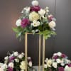Three floral arrangements with white roses, purple mums, and pale hydrangeas on gold stands