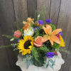 Mixed bouquet with sunflowers, orange lilies, roses, and purple blooms in a glass vase