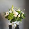 White and green floral arrangement in a glass vase with a white ribbon