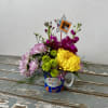 Birthday flower arrangement in a mug with pink, yellow, and green blooms
