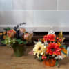 Two autumn floral arrangements in small containers, one in a pumpkin vase