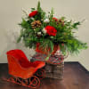 Red carnations and pinecones in a red metal sleigh with evergreens and silver ornaments beside an empty matching sleigh.