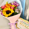 Bouquet of sunflowers, roses, and purple flowers wrapped in pink paper