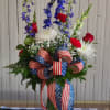 Tall red, white, and blue floral arrangement in a glass vase with patriotic ribbon