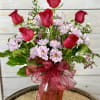 Red roses and pale pink daisies in an amber vase with a red ribbon