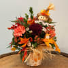 Fall floral arrangement with a scarecrow topper in a decorated vase