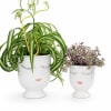 Two potted plants in white face planters with painted eyelashes and lips