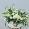 White floral arrangement in a silver vase with green accents