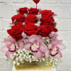 Red roses and pink orchids in a gold rectangular container with a heart pick