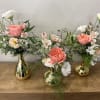 Three floral arrangements in gold vases with pink and white blooms