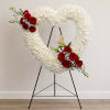 Heart-shaped white floral wreath with red rose clusters on a black stand
