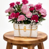 Pink carnations and roses arranged in a white handbag-shaped container