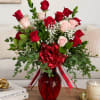 Red and pink roses arranged in a red glass vase with a ribbon bow