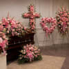 Pink funeral floral arrangements around a casket in a chapel