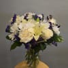 Bouquet of white daisies, cream roses, and purple filler flowers in a glass vase