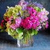 Mixed bouquet of pink blooms, green hydrangeas, and purple flowers in a clear glass cube vase
