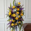 Tall funeral spray with yellow roses, white lilies, and purple flowers on a stand