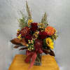 Autumn bouquet with red roses, orange blooms, and a burgundy ribbon in a glass vase