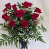 Red roses arranged in a tall silver vase with white baby's breath