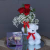 Red roses in a glass vase with a teddy bear and chocolate box