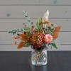 Orange and pink floral arrangement in a glass vase with a ribbon
