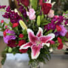 Bouquet of pink lilies, red roses, and purple flowers in a glass vase
