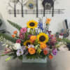 Mixed bouquet with sunflowers, roses, lilies, and daisies in a rectangular vase