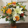 Orange roses and white lilies in a glass vase with mixed daisies