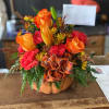 Orange and red floral arrangement in a pumpkin container with a plaid bow
