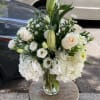 White floral arrangement in a clear glass vase with roses, lilies, and hydrangeas