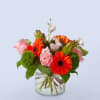 Pink roses and orange gerbera daisies in a clear glass vase