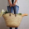 Person holding a large woven market basket with groceries and flowers