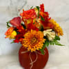 Autumn bouquet of orange roses, calla lilies, and chrysanthemums in a red vase