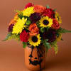 Mixed bouquet in an orange jack-o'-lantern vase with yellow and orange blooms