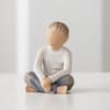 Small carved figurine of a seated child in a white shirt and blue pants