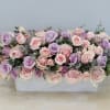 Pink and lavender roses arranged in a white rectangular container