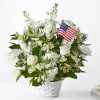 White floral arrangement in a white basket with a small American flag