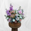 Pastel floral arrangement in a wicker basket with roses, gerbera daisies, and purple blooms