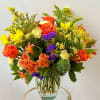 Mixed bouquet of orange roses, yellow blooms, and purple flowers in a glass vase