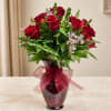 Red roses arranged in a burgundy vase with a sheer ribbon