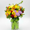 Mixed bouquet of yellow, purple, orange, and red flowers in a glass vase with a green ribbon