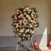 Tall standing spray of peach roses and white flowers on an easel.