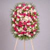 Standing oval spray of pink and white roses and carnations on an easel, framed by a ring of fanned greenery.