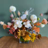 Mixed floral arrangement in a square glass vase with autumn leaves