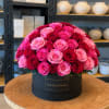 Round box arrangement of pink and red roses on a table